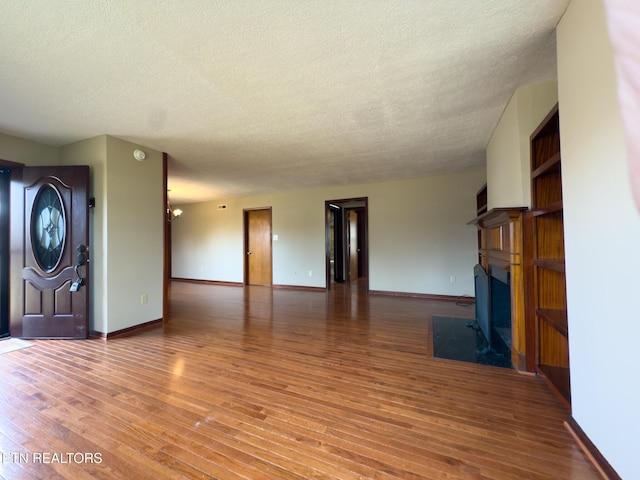 unfurnished living room with a fireplace with flush hearth, wood finished floors, baseboards, and a textured ceiling