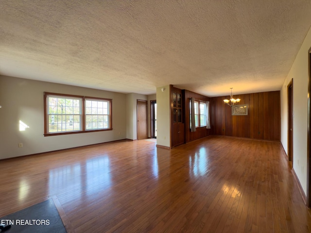 unfurnished living room with baseboards, a textured ceiling, an inviting chandelier, and hardwood / wood-style floors