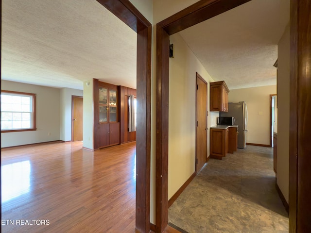 corridor featuring light wood-style floors, baseboards, and a textured ceiling