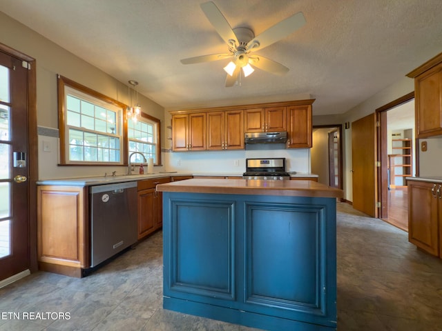 kitchen with a ceiling fan, a kitchen island, stainless steel appliances, light countertops, and under cabinet range hood