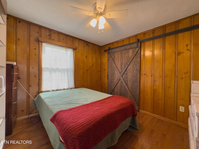 bedroom featuring wooden walls, wood finished floors, baseboards, a textured ceiling, and a barn door