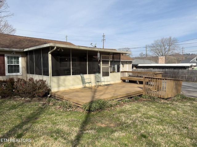 back of house with fence, roof with shingles, a lawn, a deck, and a sunroom