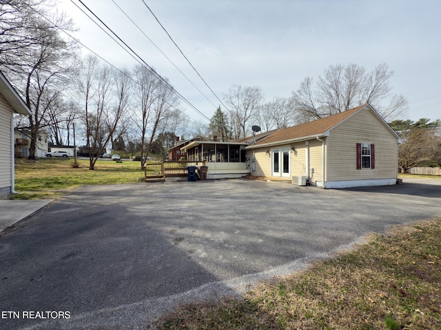 view of side of property featuring aphalt driveway, central AC, and a sunroom