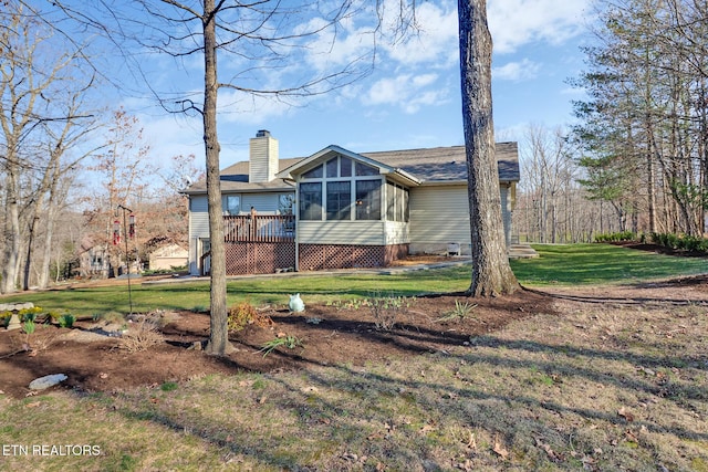 rear view of property featuring roof with shingles, a yard, a sunroom, a chimney, and a deck