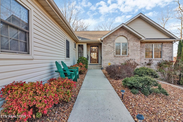 property entrance featuring brick siding and roof with shingles