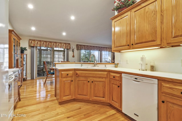 kitchen with light wood-type flooring, a sink, a peninsula, white dishwasher, and light countertops