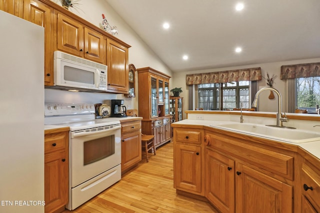 kitchen featuring brown cabinets, light wood-style flooring, a sink, white appliances, and light countertops