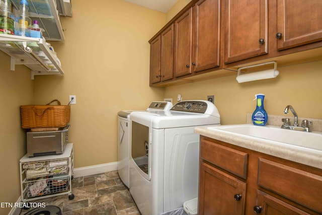 laundry area with washing machine and clothes dryer, stone finish flooring, baseboards, cabinet space, and a sink