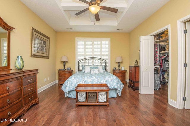 bedroom with dark wood-style floors, a walk in closet, a raised ceiling, and baseboards