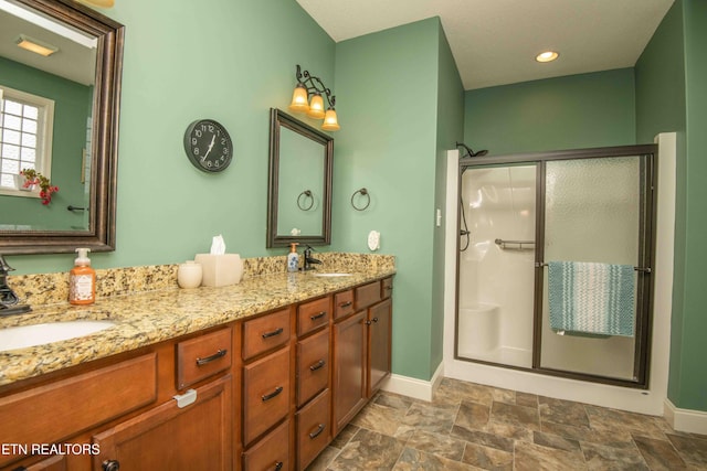 full bath featuring stone finish floor, a stall shower, baseboards, and a sink