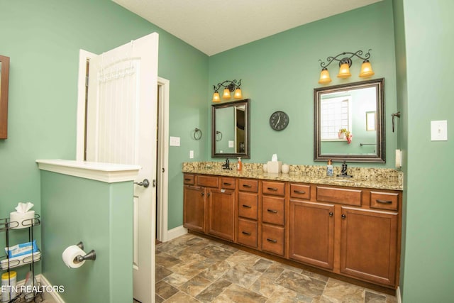 bathroom featuring a sink, stone finish flooring, baseboards, and double vanity