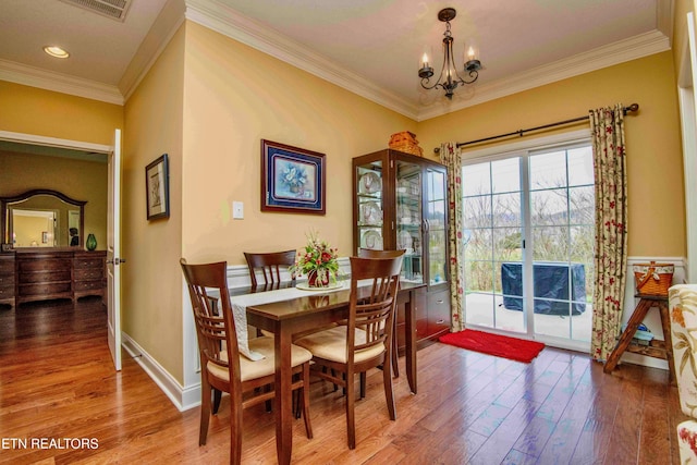 dining room with wood finished floors, baseboards, ornamental molding, and an inviting chandelier