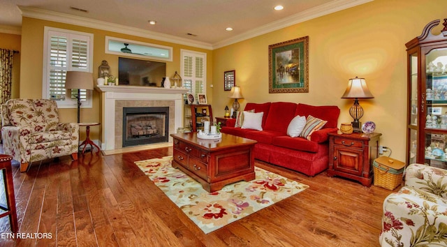 living area featuring a tile fireplace, wood finished floors, visible vents, and crown molding