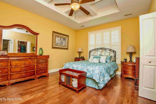 bedroom with wood finished floors, ceiling fan, baseboards, coffered ceiling, and visible vents