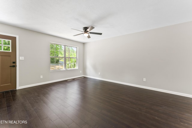 spare room featuring dark wood-style flooring, a ceiling fan, baseboards, and a healthy amount of sunlight