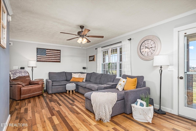 living room with light wood-type flooring, ornamental molding, a ceiling fan, a textured ceiling, and baseboards