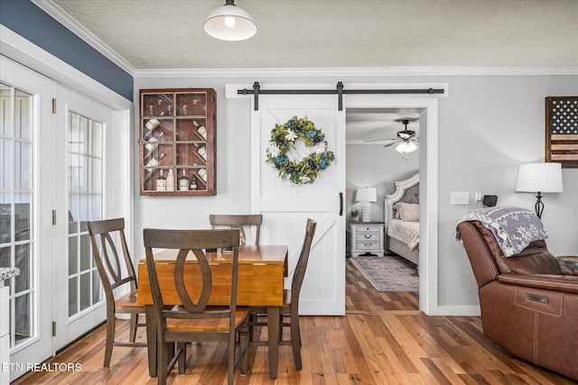 dining room featuring ornamental molding, a textured ceiling, a barn door, and wood-type flooring