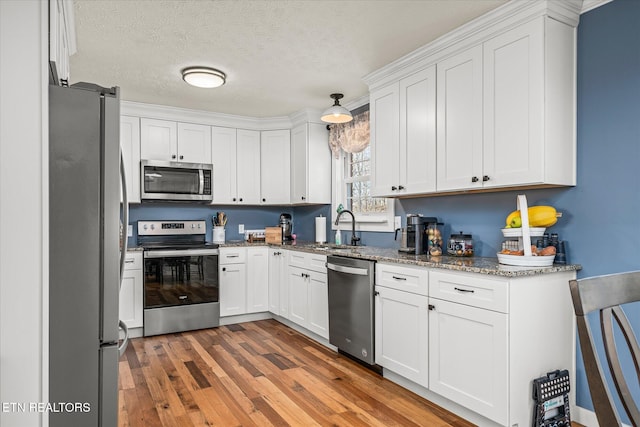 kitchen featuring appliances with stainless steel finishes, white cabinetry, light wood-type flooring, and a sink