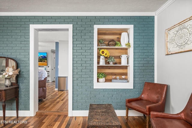 sitting room featuring a textured ceiling, brick wall, wood finished floors, and crown molding