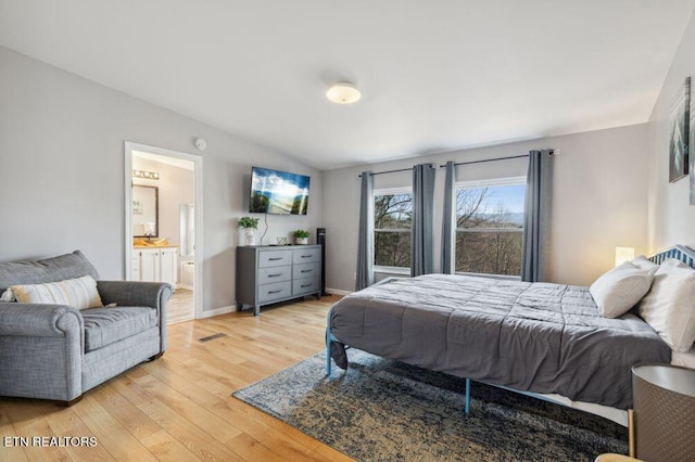 bedroom with connected bathroom, light wood-type flooring, baseboards, and vaulted ceiling