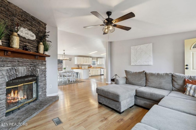 living room with visible vents, baseboards, a fireplace, light wood-style floors, and a ceiling fan