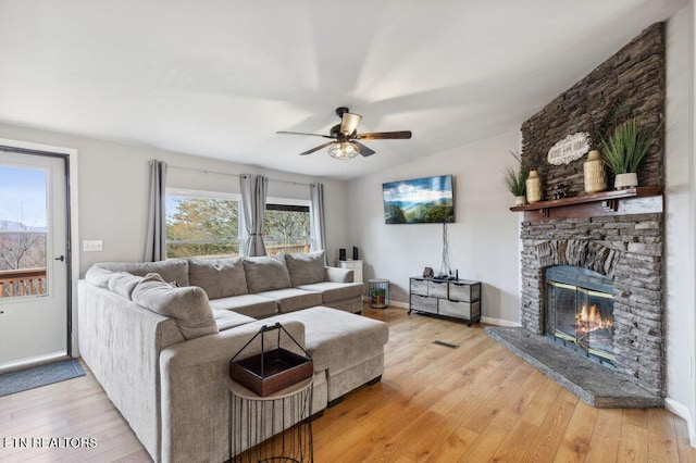 living room with lofted ceiling, a stone fireplace, light wood finished floors, baseboards, and ceiling fan