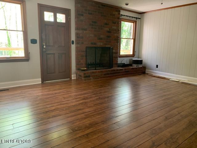 unfurnished living room with visible vents, baseboards, wood-type flooring, crown molding, and a brick fireplace