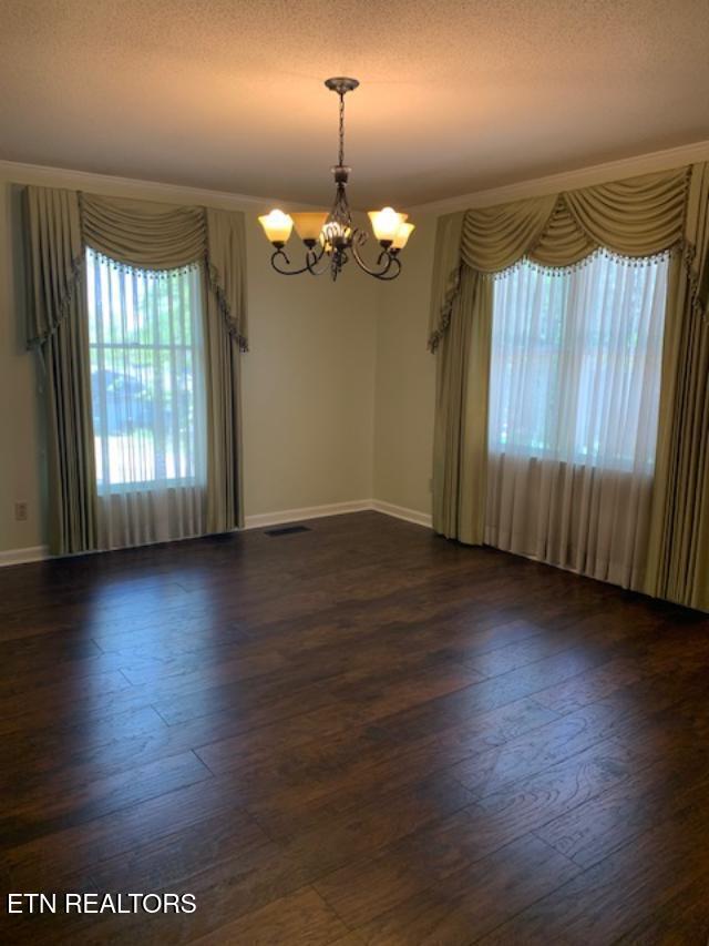 empty room featuring a notable chandelier, dark wood-style floors, and a textured ceiling