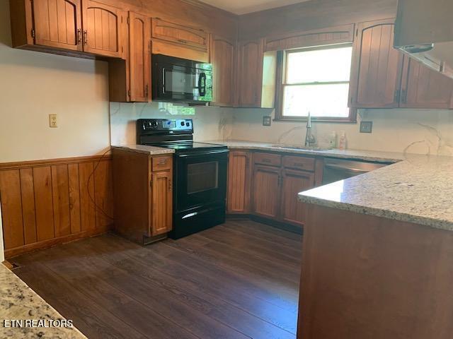 kitchen with wainscoting, brown cabinets, dark wood-style floors, black appliances, and a sink