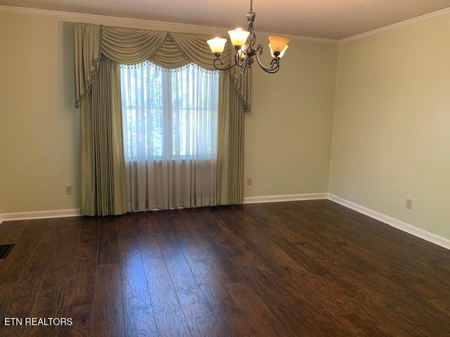 unfurnished room featuring an inviting chandelier, dark wood-style floors, crown molding, and baseboards