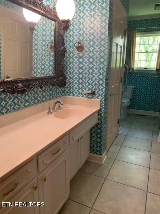 bathroom with vanity, baseboards, wallpapered walls, tile patterned floors, and toilet