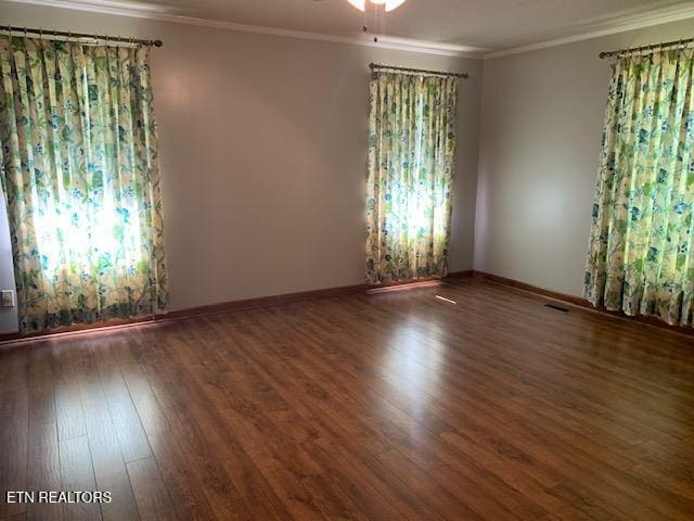 spare room with crown molding, wood finished floors, visible vents, and baseboards