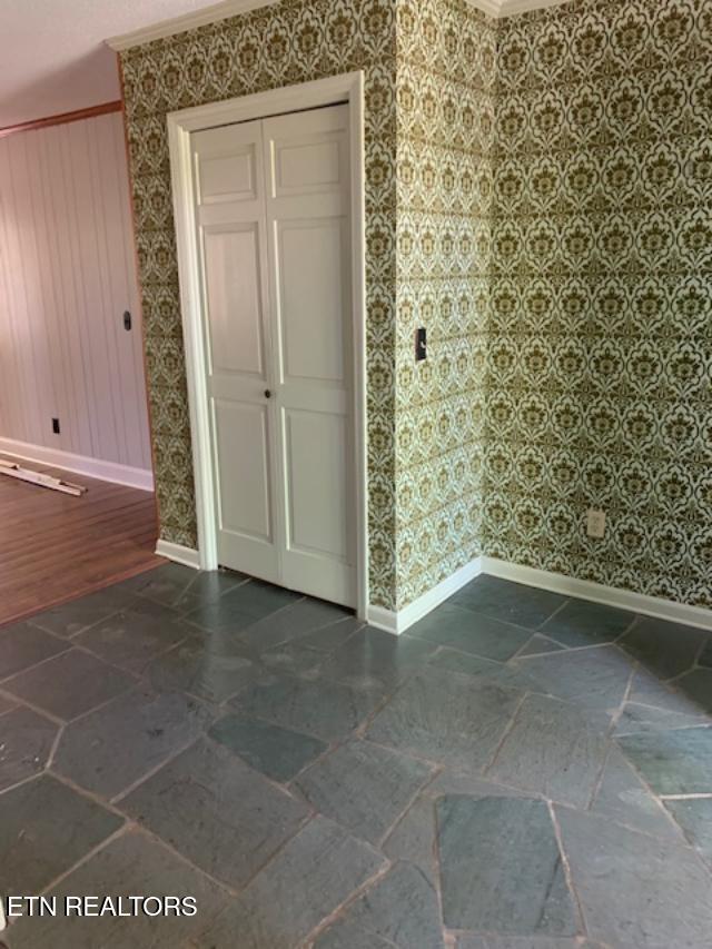 spare room featuring baseboards, crown molding, and wallpapered walls