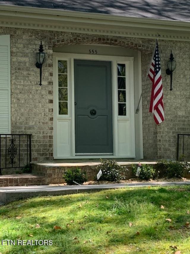 doorway to property featuring covered porch, brick siding, and roof with shingles