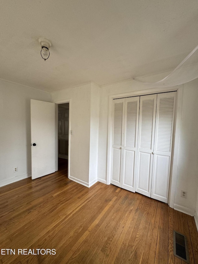 unfurnished bedroom with wood finished floors, visible vents, a closet, and baseboards