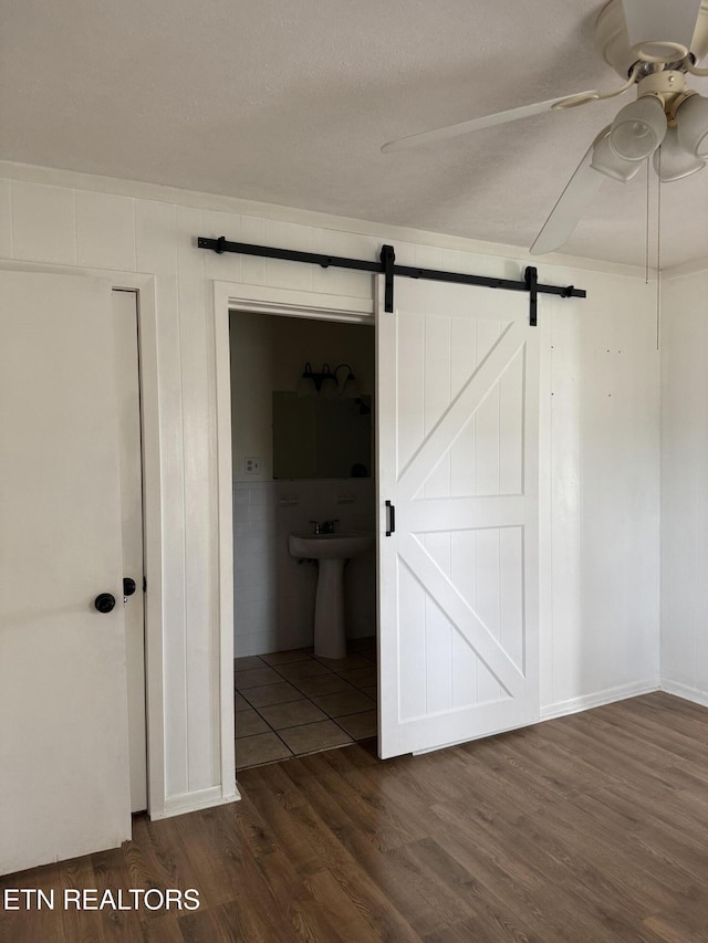 unfurnished bedroom with a ceiling fan, a sink, a textured ceiling, dark wood finished floors, and a barn door