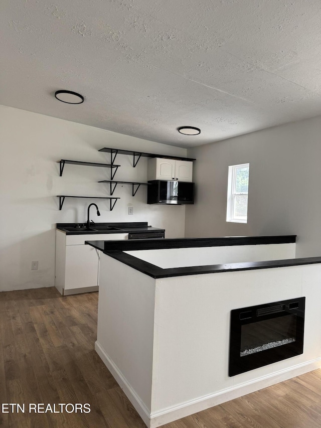 kitchen featuring dark countertops, wood finished floors, open shelves, a sink, and stainless steel microwave