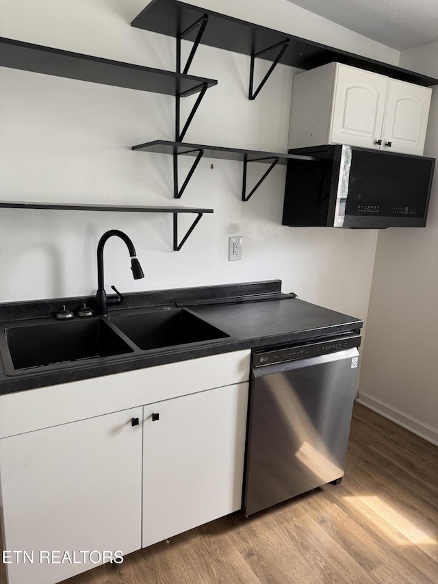 kitchen featuring a sink, dark countertops, white cabinets, light wood finished floors, and dishwasher