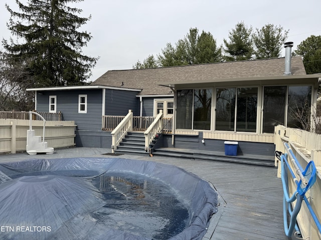 rear view of property featuring a shingled roof, fence, a sunroom, and a wooden deck