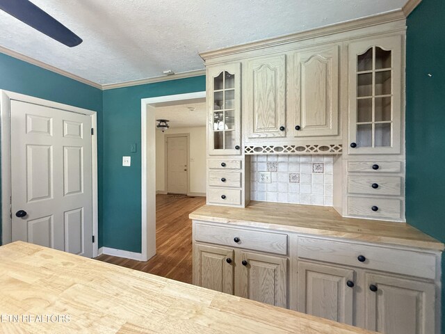 kitchen featuring tasteful backsplash, a textured ceiling, cream cabinetry, glass insert cabinets, and wood finished floors