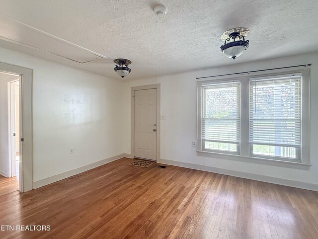 empty room featuring baseboards, attic access, light wood finished floors, and a wealth of natural light