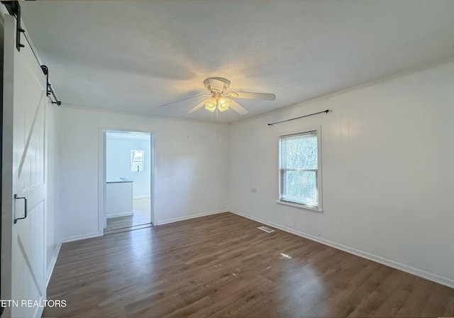 spare room with baseboards, a barn door, wood finished floors, and ceiling fan