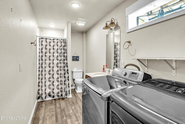 clothes washing area with wood finished floors, baseboards, laundry area, a sink, and washing machine and dryer