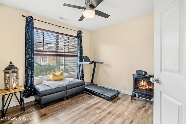 exercise room featuring a wood stove, baseboards, wood finished floors, and a ceiling fan