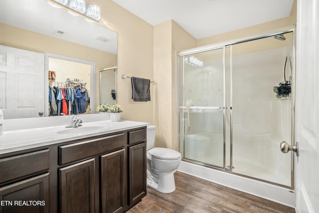 full bath with a shower stall, a walk in closet, toilet, wood finished floors, and vanity