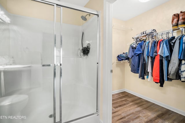 full bath with wood finished floors, baseboards, a shower stall, a walk in closet, and toilet