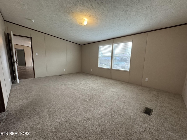 spare room with carpet flooring, a textured ceiling, crown molding, and visible vents