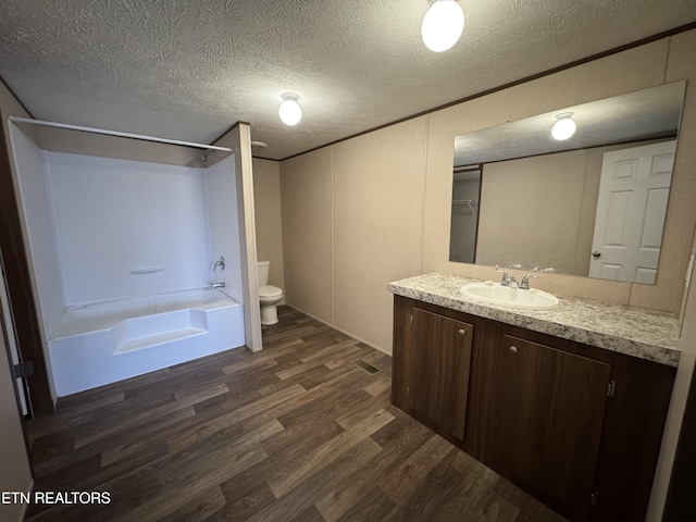 full bath with vanity, a textured ceiling, wood finished floors, shower / bath combination, and toilet