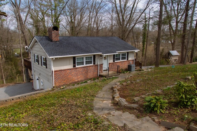 single story home featuring central air condition unit, brick siding, a chimney, and a shingled roof