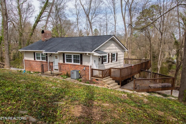 view of front of property with a deck, cooling unit, a shingled roof, brick siding, and a chimney